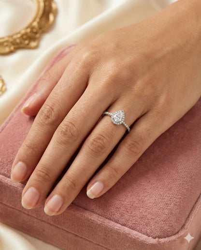 Teardrop White Topaz ring with halo setting and pave silver band on black background.