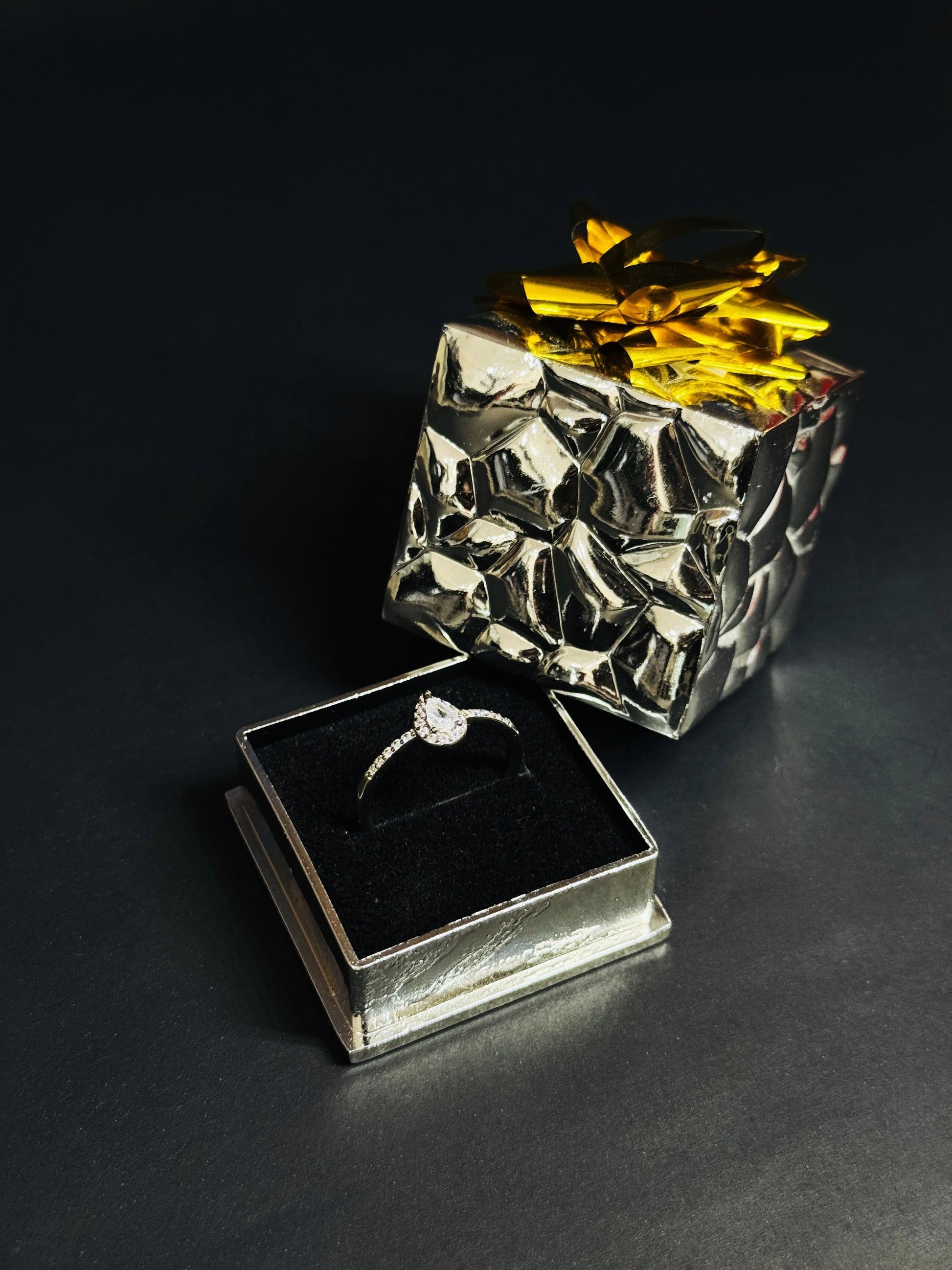 Teardrop White Topaz ring with halo setting and pave silver band on black background.